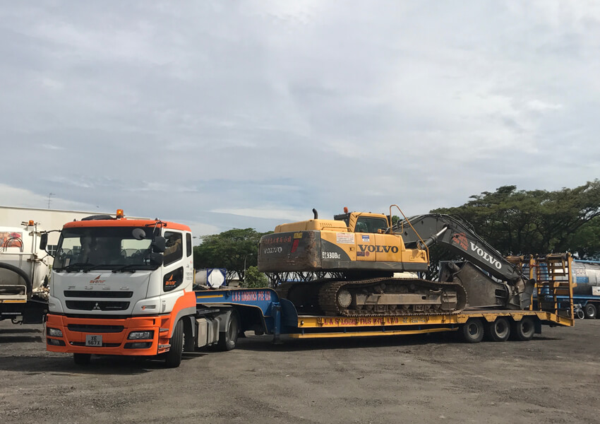 Avenir Logistics truck transporting a Volvo excavator on a flatbed trailer.