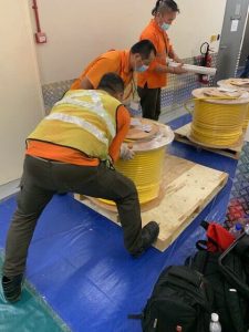 Workers handling yellow industrial cable reels for installation at a site.